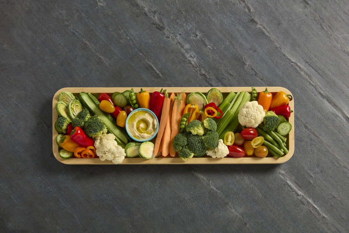 Top-down view of a bamboo cutting board loaded with vegetables on a dark slate surface