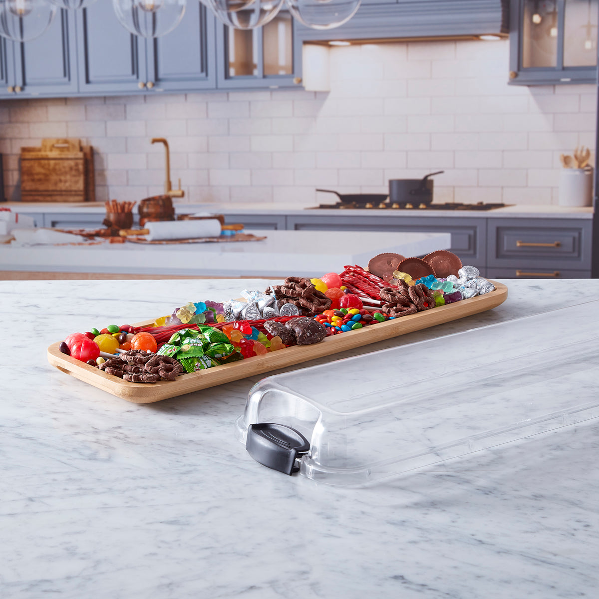 Build-a-Board bamboo cutting board brimming with colorful candy and fruit on a marble kitchen island with blue cabinets.