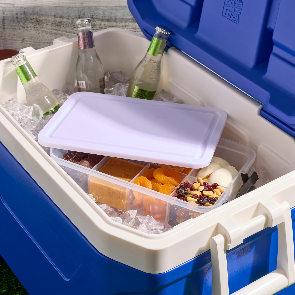 Snacklebox open on a kitchen shelf with clear compartments holding dried fruit nuts and orange slices