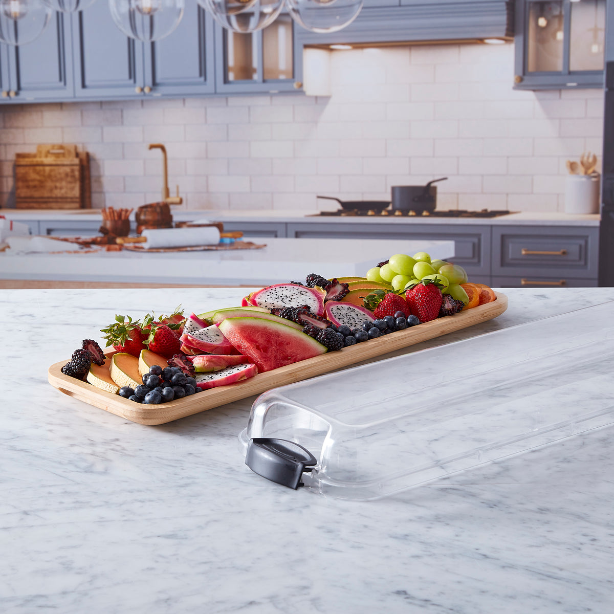 Assorted fruit platter on a long bamboo cutting board atop a marble kitchen island.
