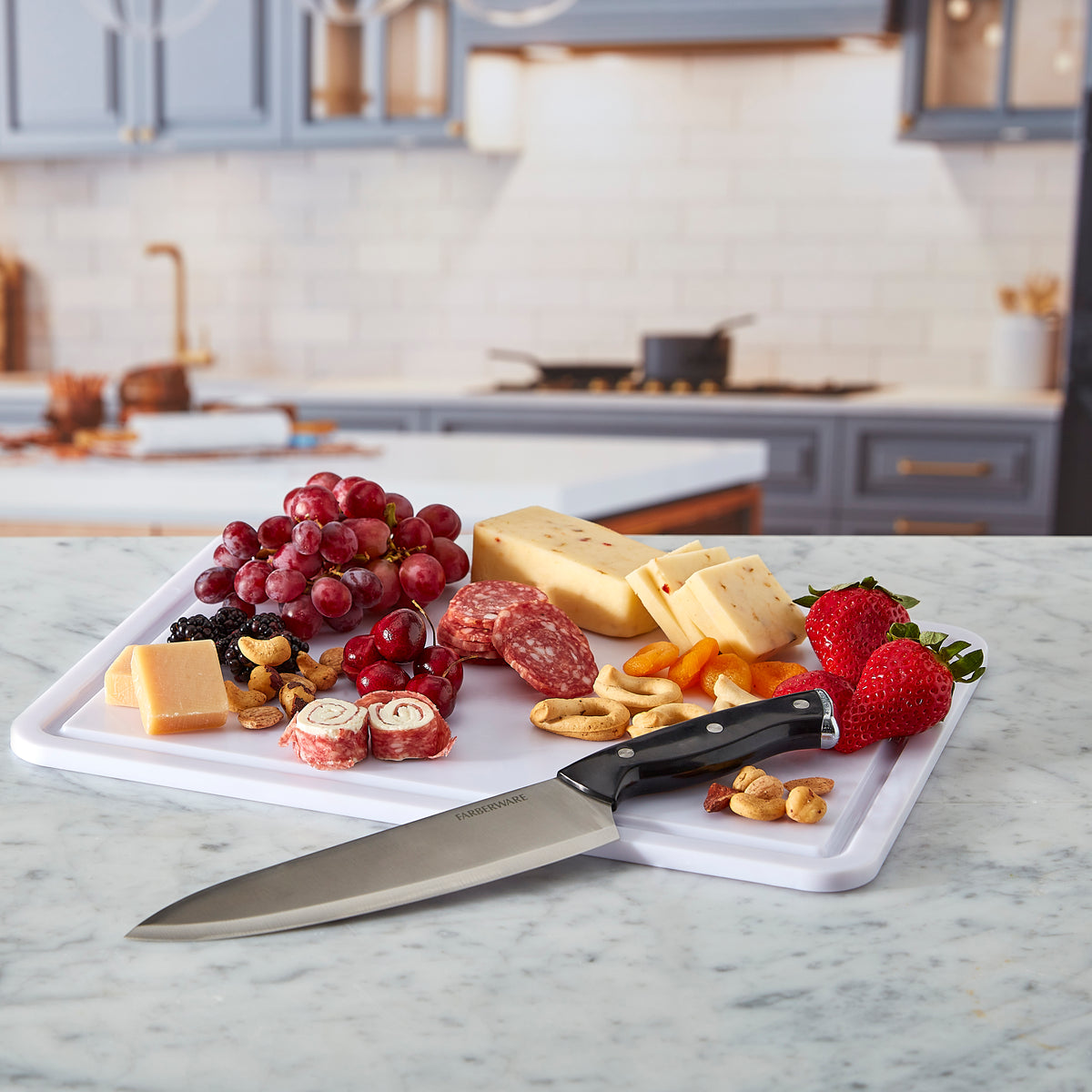 Open Snacklebox with cookies crackers cheese and grapes plus a kitchen knife nearby on a marble surface