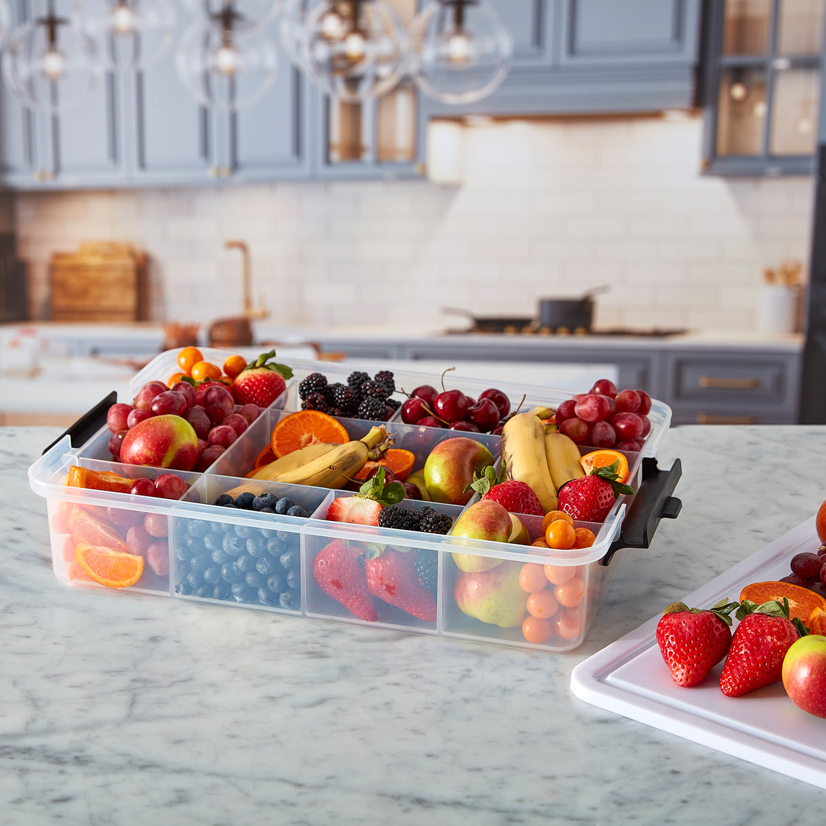 Assorted fresh fruit arranged in a clear multi compartment Snacklebox on a marble kitchen counter